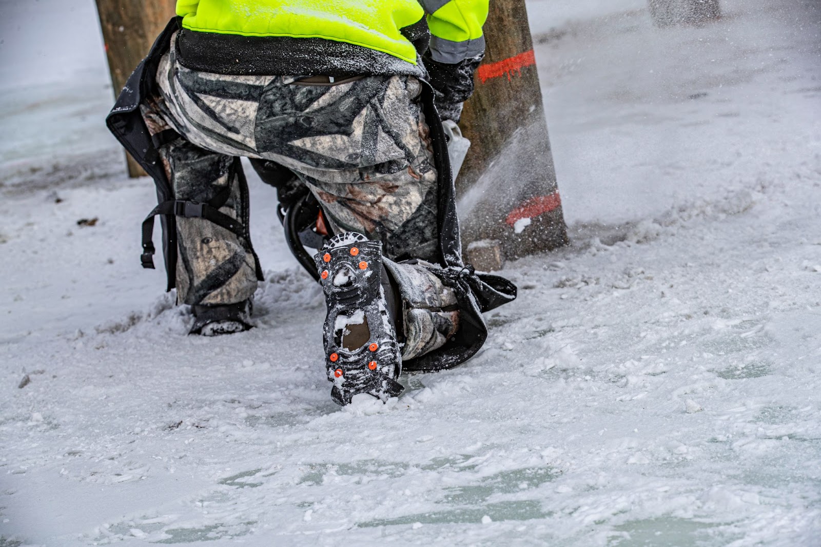 Worker wearing ice cleat while kneeling and completing work in the snow